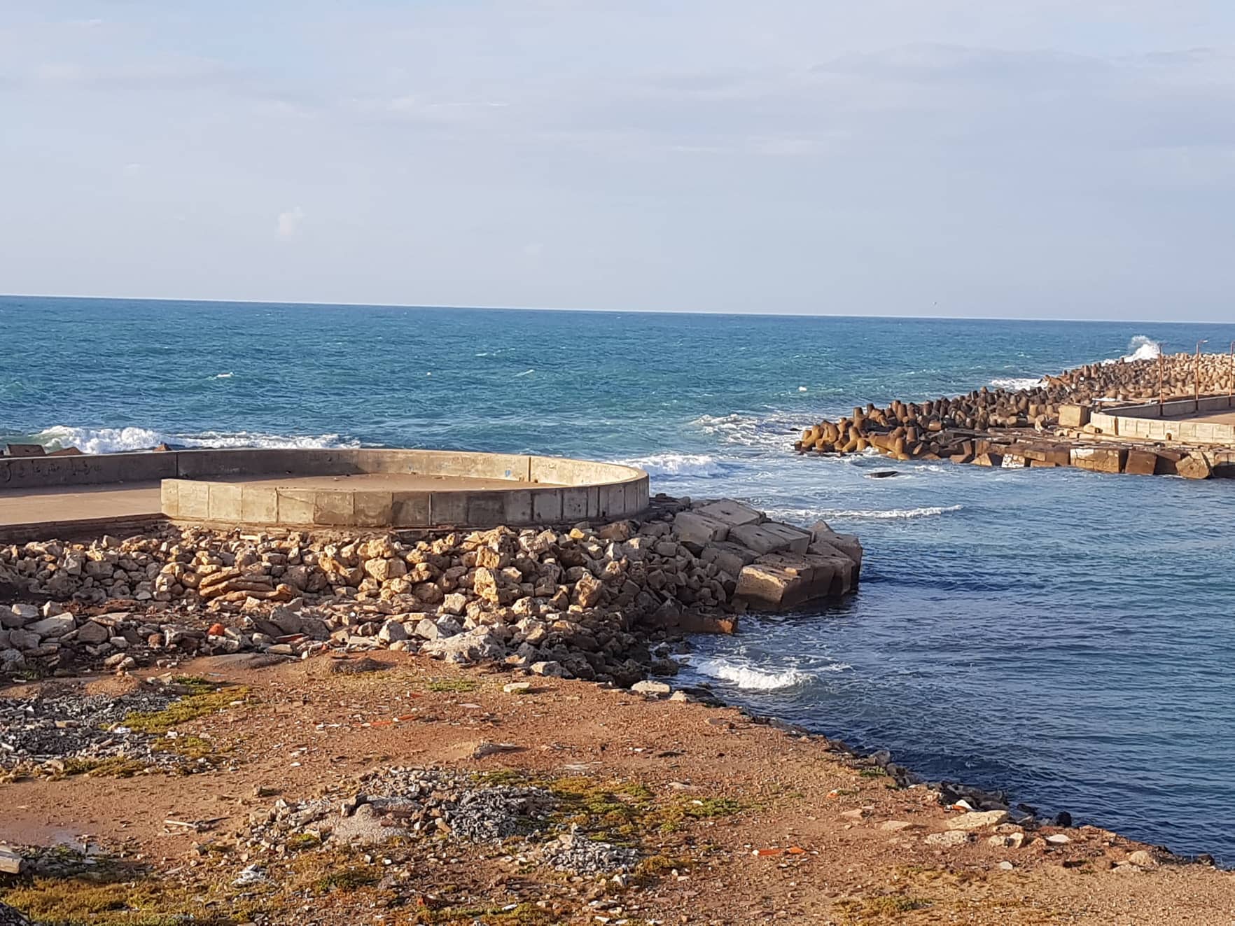 صخور بئر مسعود على حافة البحر، ودائرة البئر الحجرية وكاسر الأمواج خلفها