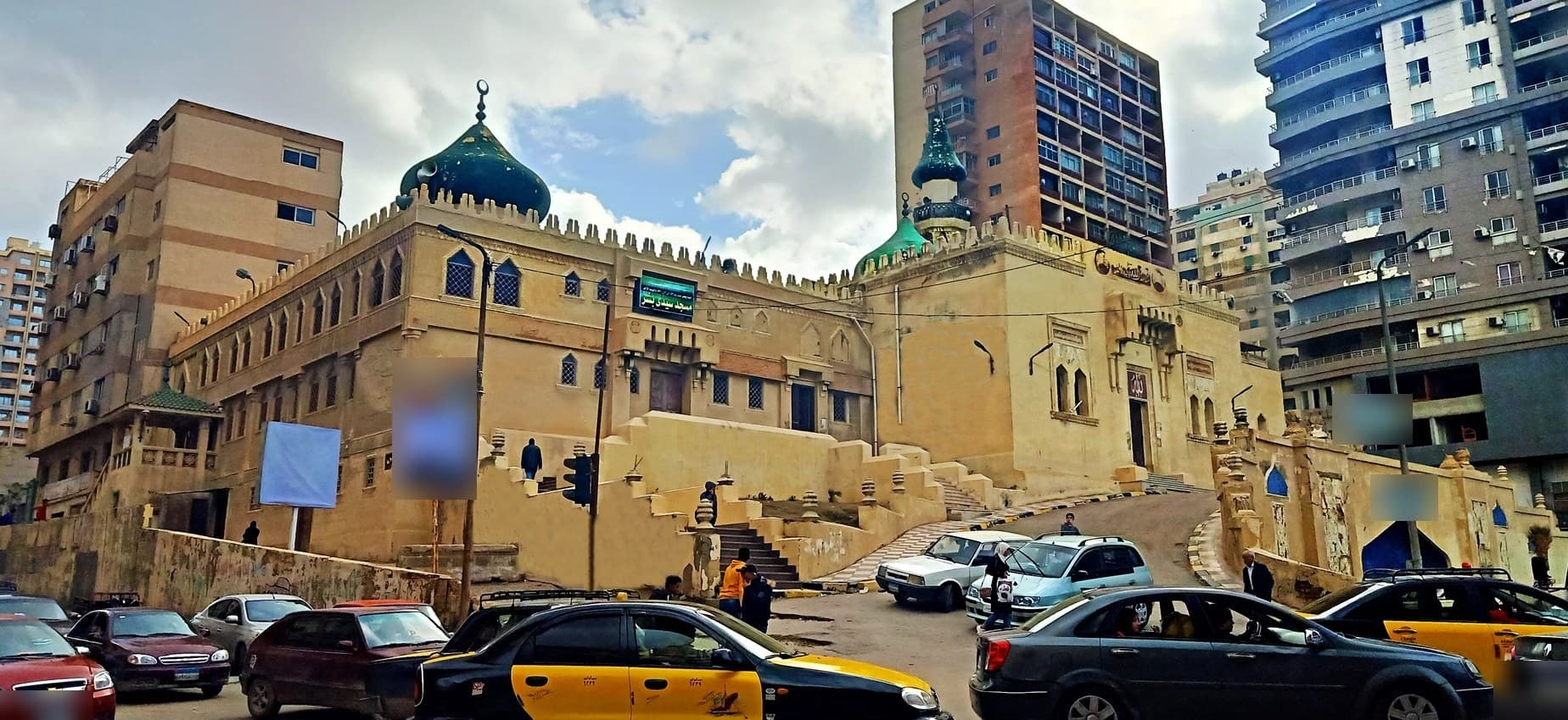 مسجد سيدي بشر بقبتيه الخضراوين وأسواره المسننة، والدرج الصاعد إلى مدخله فوق الشارع